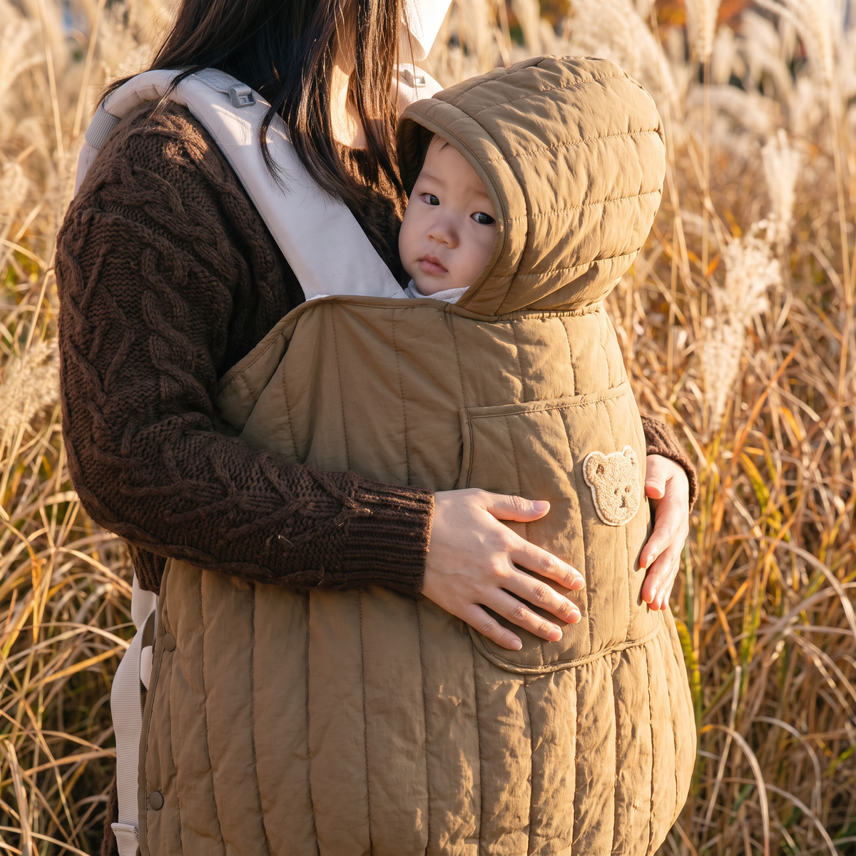 Mother carrying her baby outdoors in the camel quilted babywearing cover — Orla Babywearing Cover — NAEVII#Color_Camel