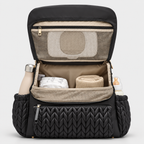 NAEVII Elara Diaper Bag Backpack in black, open front view showing beige lining, zippered mesh pocket inside the flap, main compartment with diaper and blanket, and side pockets holding a flask and baby bottle#Color_Black