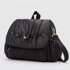 NAEVII Elara Diaper Bag Backpack in black, three-quarter side view with quilted flap, gold-tone drawstring clasp and detachable shoulder strap#Color_Black