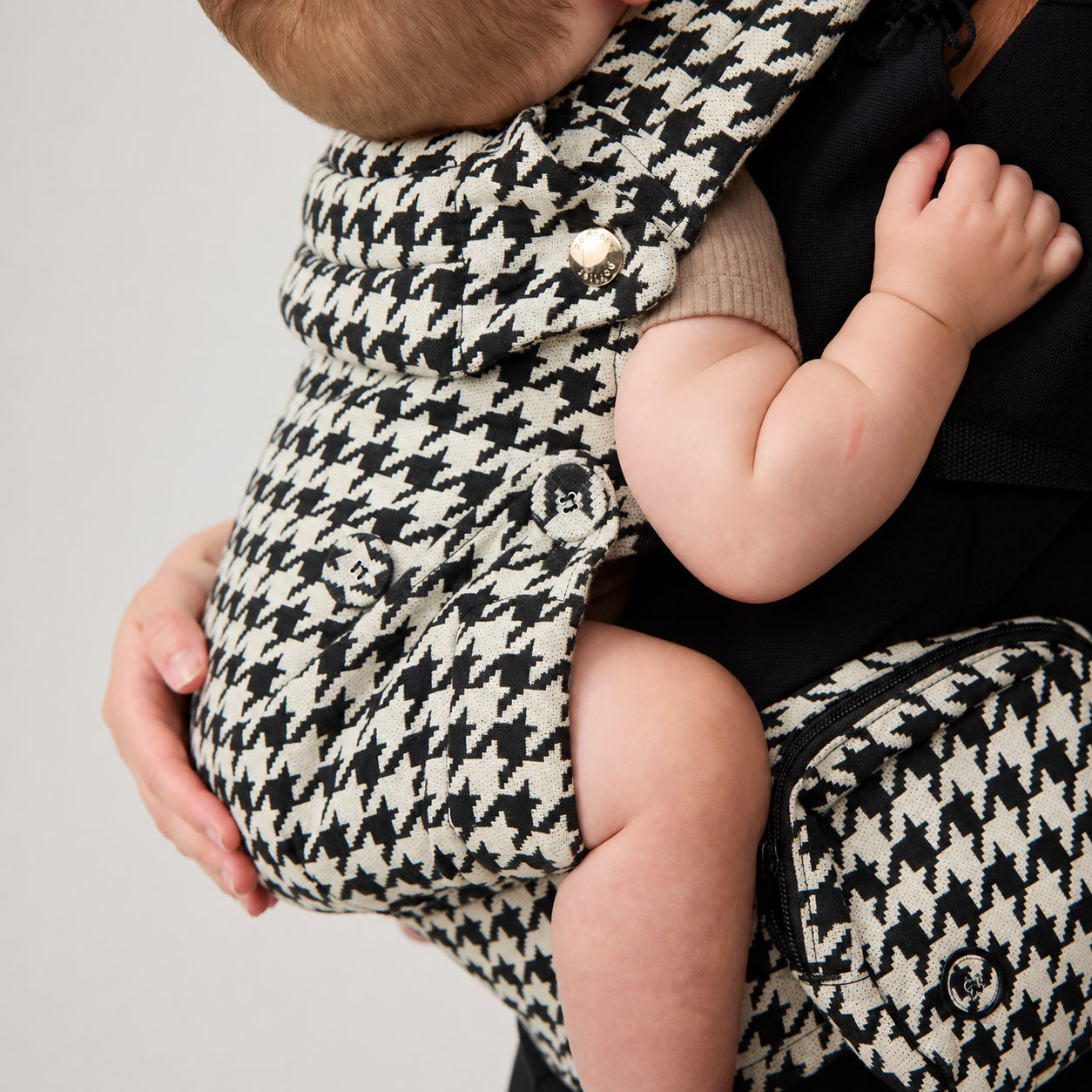 Baby seated in NAEVII Limitless Baby Carrier, black and white Houndstooth, close up of seat and zip pocket#Color_Houndstooth