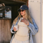 Woman holding a coffee outdoors while carrying newborn in NAEVII Soft Baby Carrier, beige Cream#Color_Cream