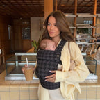 Woman at a cafe carrying newborn in NAEVII Soft Baby Carrier, black Onyx Houndstooth#Color_Onyx Houndstooth