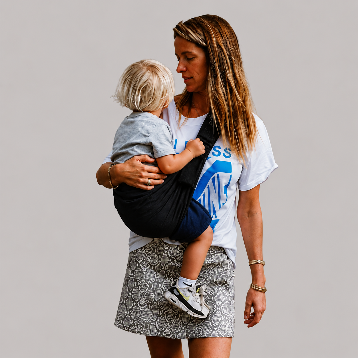Woman carrying her toddler in the NAEVII Toddler Sling Carrier in black, worn on the side with the child facing her#Color_Black