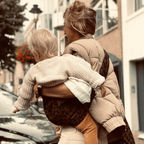Woman carrying her toddler in the NAEVII Toddler Sling Carrier, brown leopard print, walking on a city street seen from behind#Color_Brown Leopard