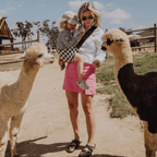 Woman feeding alpacas while carrying her toddler in the NAEVII Toddler Sling Carrier, black and white Houndstooth, outdoors at a farm#Color_Houndstooth