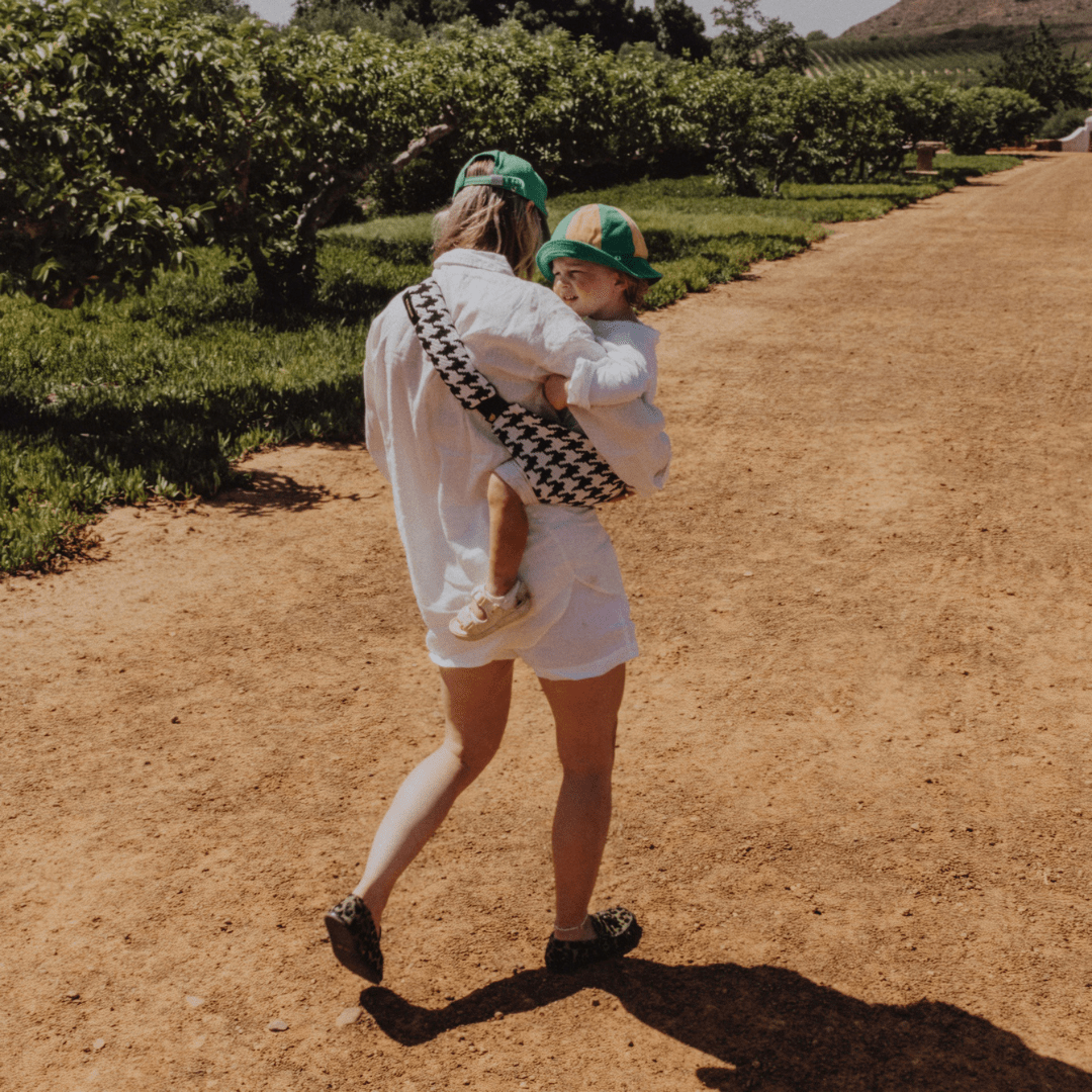 Woman walking a country path carrying her toddler in the NAEVII Toddler Sling Carrier, black and white Houndstooth, seen from behind#Color_Houndstooth
