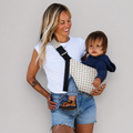Woman carrying her toddler in the NAEVII Toddler Sling Carrier, Neutral Houndstooth, front carry with padded shoulder strap#Color_Neutral Houndstooth